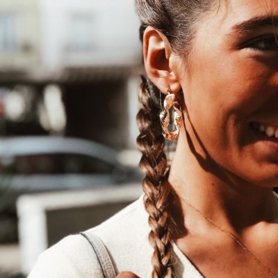 Brincos dourados geométricos em mulher com cabelo trançado