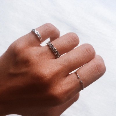 Mão com três anéis de prata de estilos variados em fundo branco