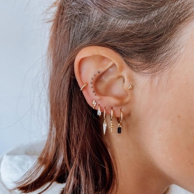 Orelha com vários brincos de argola dourados com pendentes variados