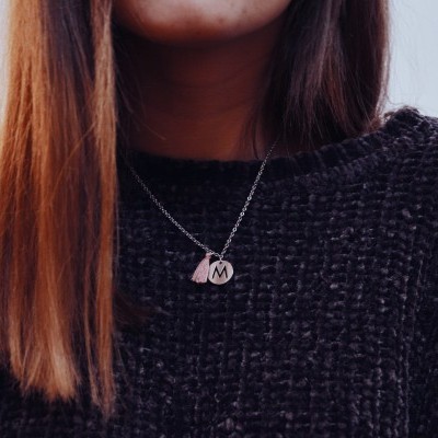 Colar prateado com pendentes, letra M e rosa, usado com camisola preta.