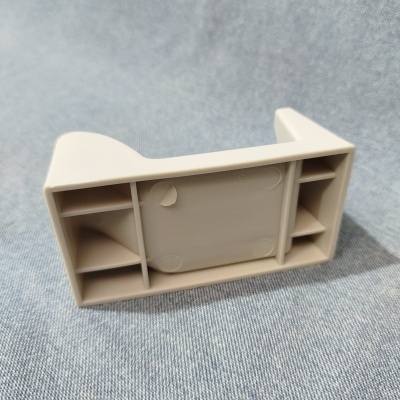 Peça plástica cinza com compartimentos retangulares sobre tecido cinzento