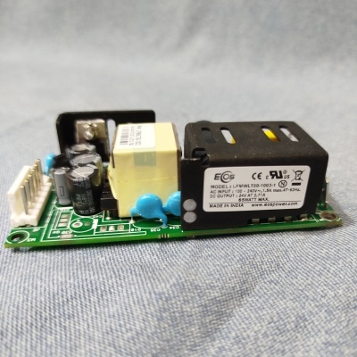 Placa eletrónica com transformador amarelo e caixa preta sobre tecido azul