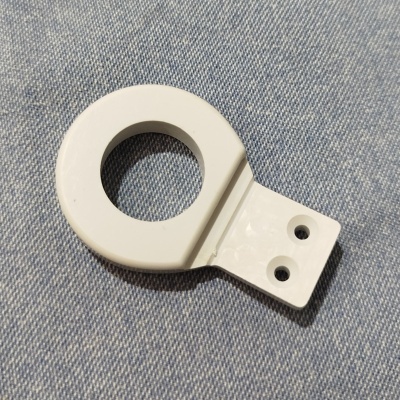 Peça plástica branca circular com dois orifícios em fundo de tecido azul-claro