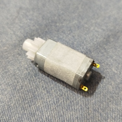 Motor pequeno metálico com caixa de engrenagens branca sobre tecido azul