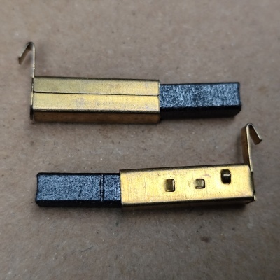 Dois escovas de carvão metálicas douradas com ponta preta sobre superfície castanha