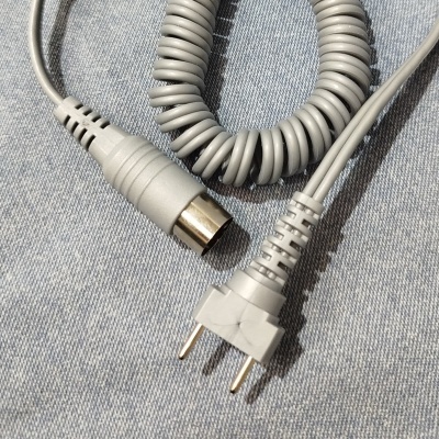 Cabo elétrico cinzento com conector de duas pontas e conector redondo, sobre tecido azul