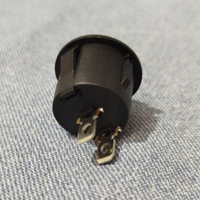 Peça eletrónica preta com terminais metálicos sobre tecido azul claro