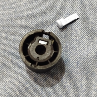 Peça de plástico preta redonda com componente branco sobre tecido azul