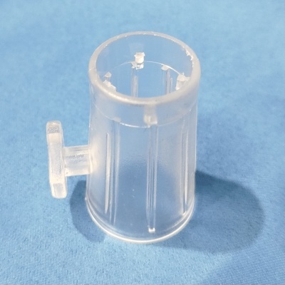 Peça plástica transparente cilíndrica com aba lateral sobre tecido azul