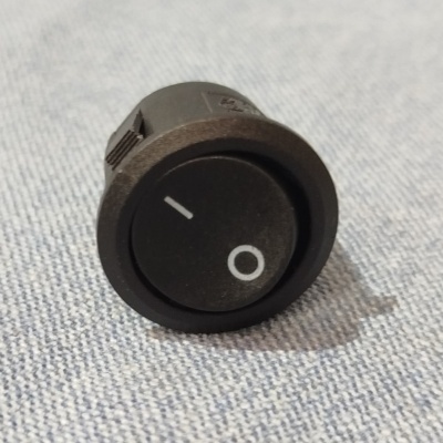 Interruptor redondo preto com símbolos I e O num tecido cinza claro