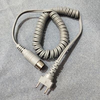 Cabo elétrico cinzento enrolado com conector circular e ficha de três pinos sobre tecido azul-claro