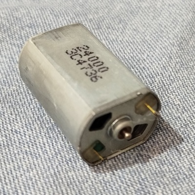 Motor elétrico pequeno de metal com texto SUN 34000 514736 sobre tecido cinza claro