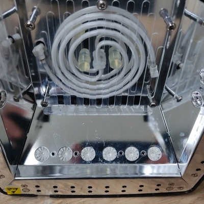 Aparelho metálico com espelho, elemento espiral branco e botões prateados sobre madeira