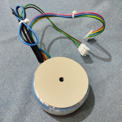 Transformador toroidal metálico com fios coloridos e conectores brancos num tecido azul.