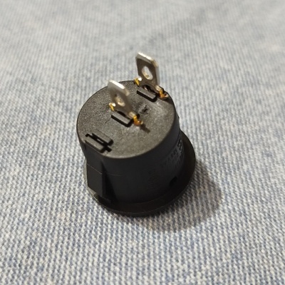 Peça eletrónica preta redonda com terminais metálicos em tecido azul claro