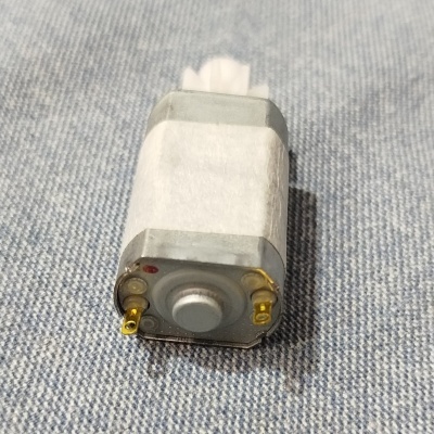 Motor elétrico pequeno cinza e branco com terminais dourados sobre tecido azul claro