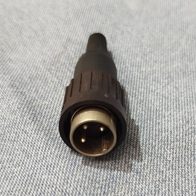Conector preto com três pinos metálicos sobre tecido cinzento