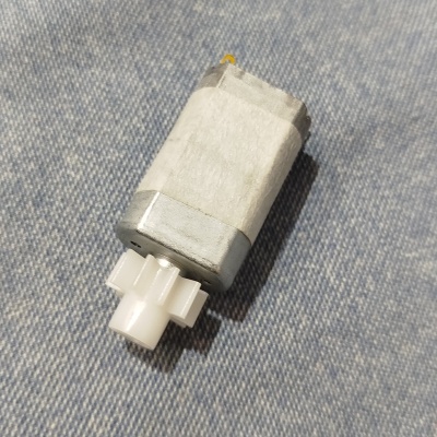 Motor elétrico pequeno com engrenagem branca sobre tecido azul semelhante a ganga