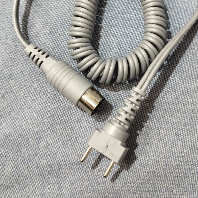 Cabo elétrico cinzento com conector de duas pontas e conector redondo, sobre tecido azul