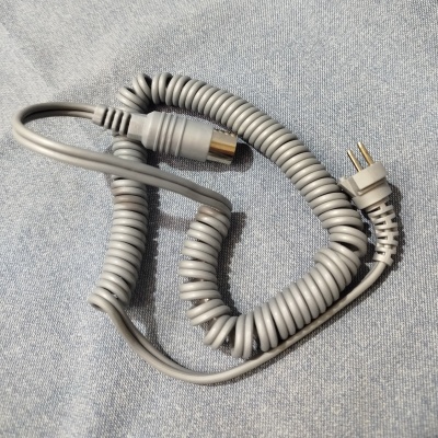 Cabo cinzento enrolado com plugue e conector coaxial sobre tecido cinzento.