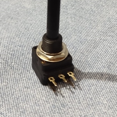 Interruptor toggle de três terminais, alavanca preta, base preta, tecido cinza ao fundo