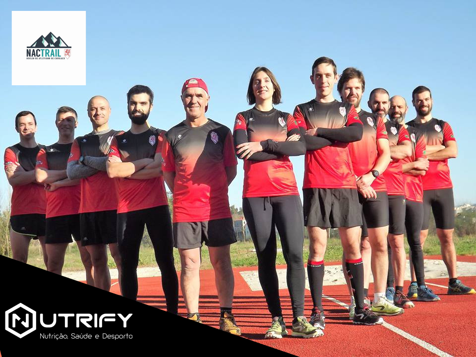 Grupo de corredores com uniformes vermelhos e pretos numa pista de corrida ao ar livre.
