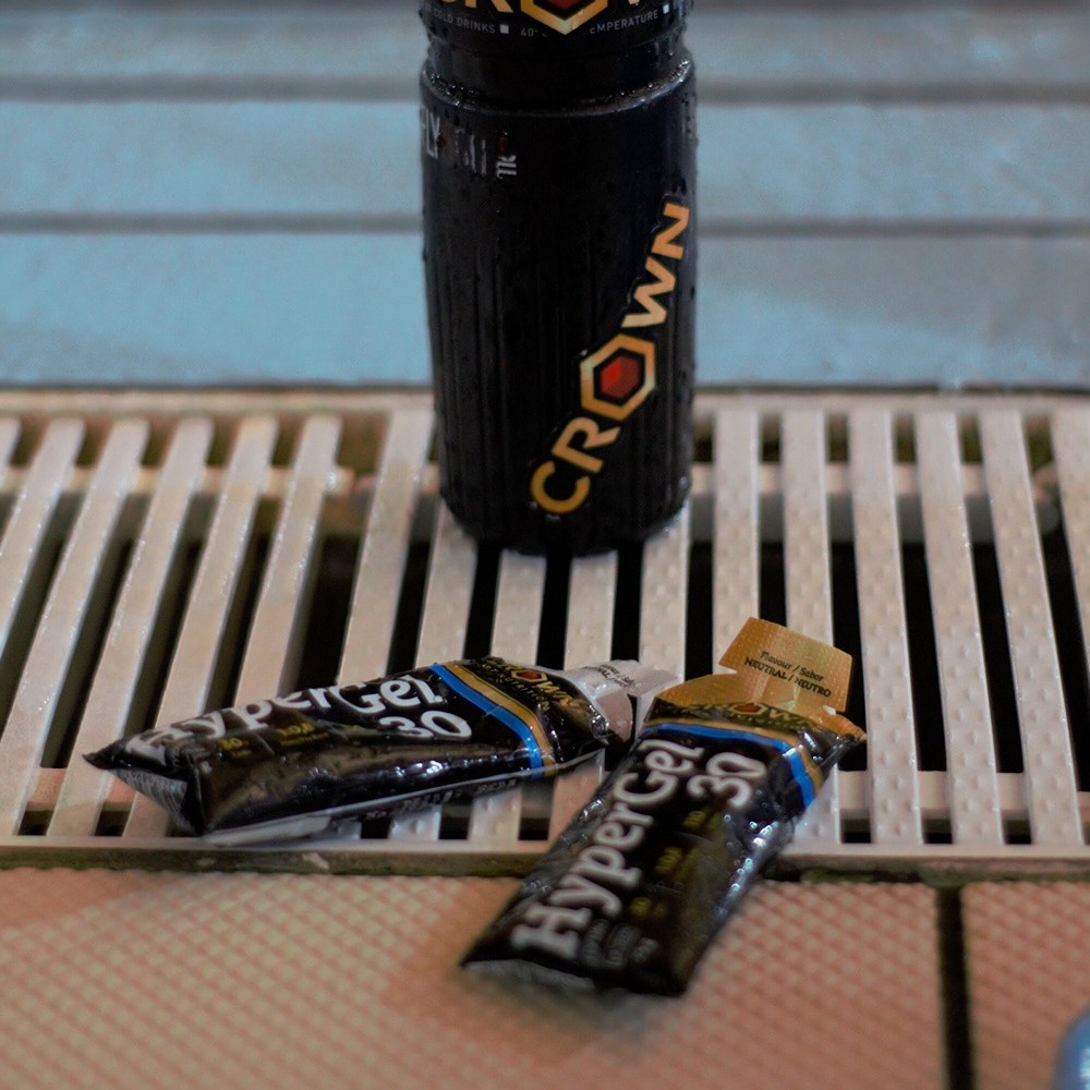 Garrafa preta CROWN e dois géis energéticos Hypergel 30 numa superfície branca