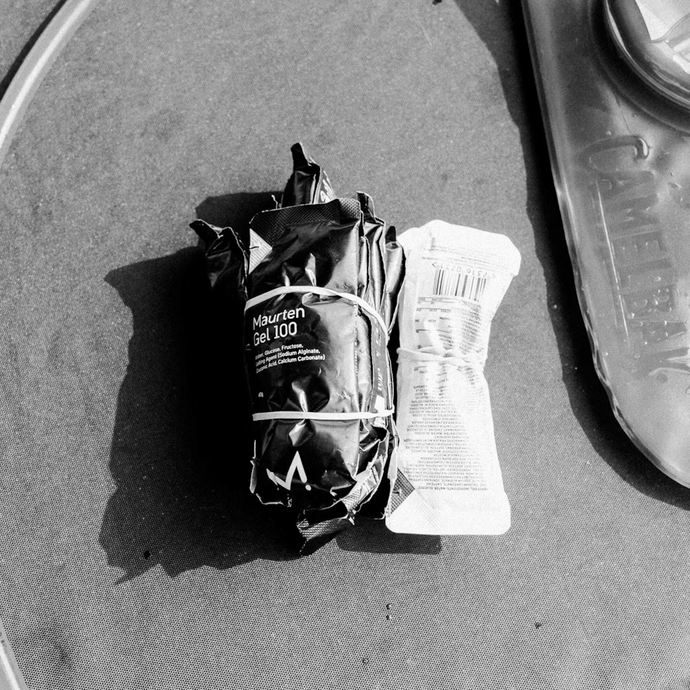 Pacote preto e branco de gel energético Maurten Gel 100 sobre superfície escura com peça plástica translúcida
