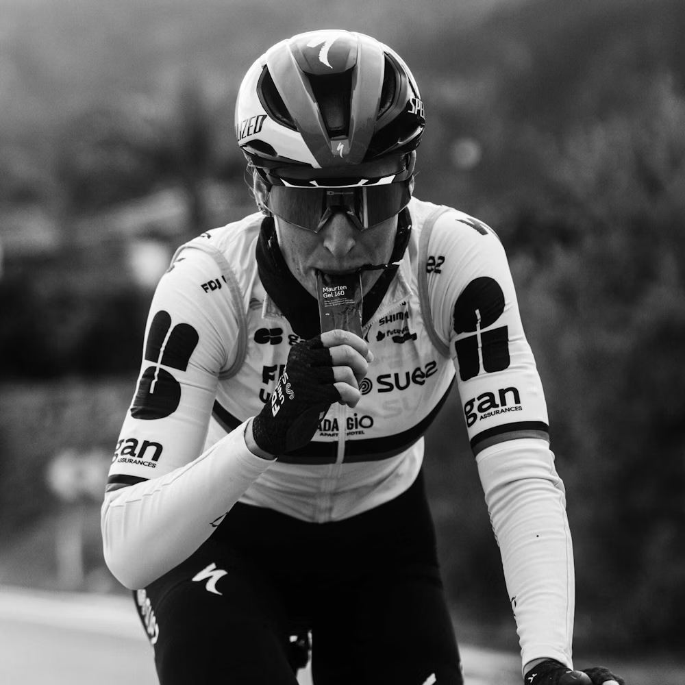 Ciclista com capacete e óculos a comer gel energético durante treino.