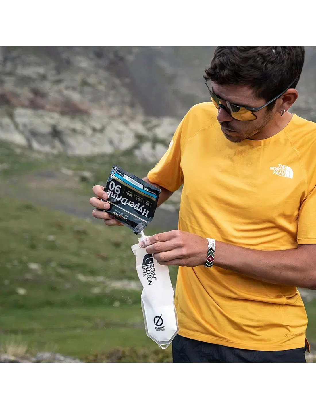 Homem a verter suplemento Hyporoman 90 para recipiente The North Face em montanha