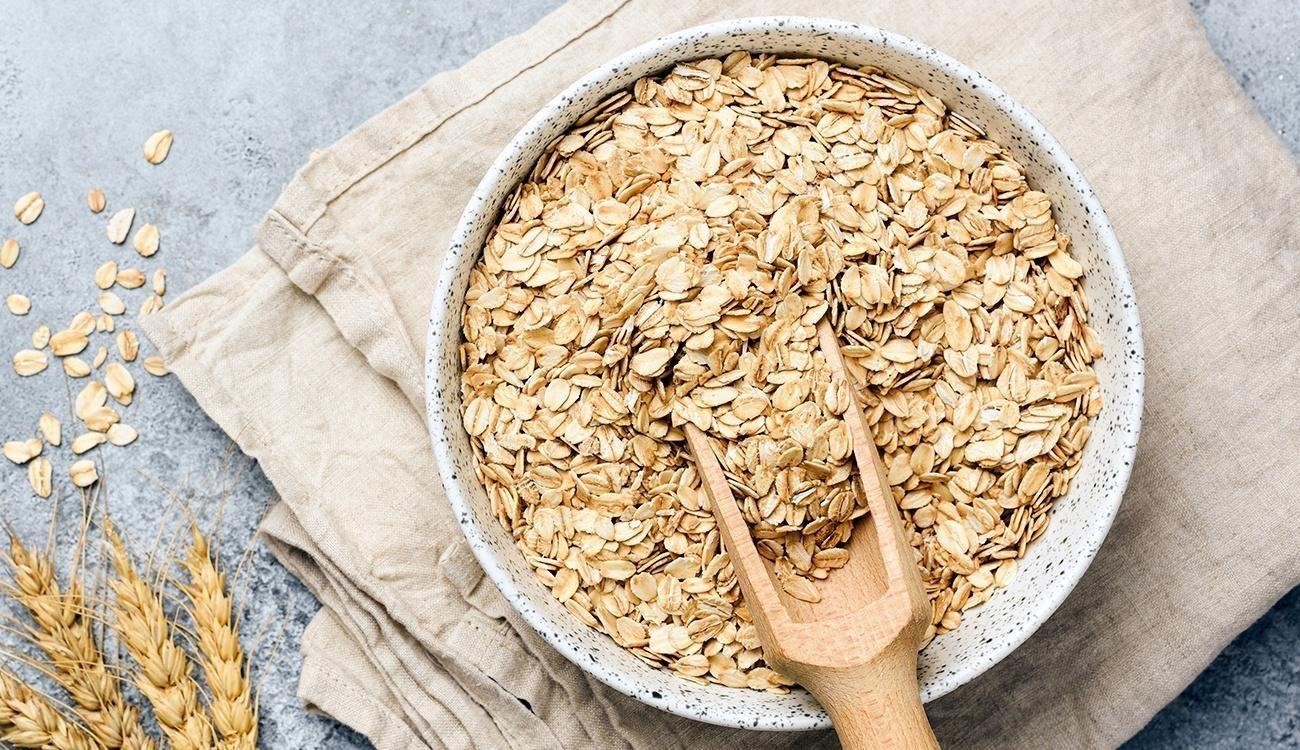 Taça branca com flocos de aveia e colher de madeira em pano bege