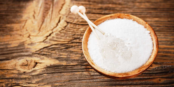 Recipiente de madeira com sal grosso branco e espetos de cristal sobre superfície de madeira rústica