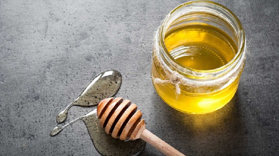 MEL: ALIMENTO NATURAL COMO FONTE DE ENERGIA Frasco de vidro com mel e colher de madeira sobre superfície cinzenta