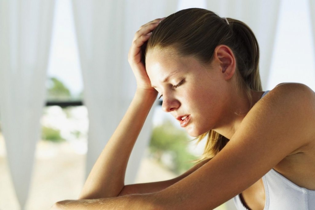 Mulher com camisola branca, mão na cabeça, interior iluminado pela luz do dia