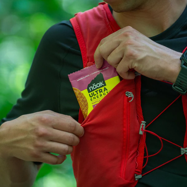 Pessoa a colocar snack Naak Ultra Energy no bolso de colete desportivo vermelho
