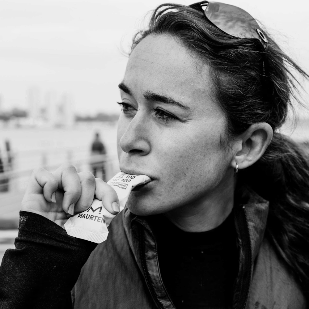 Mulher com casaco técnico a morder pacote branco MAURTEN ao ar livre