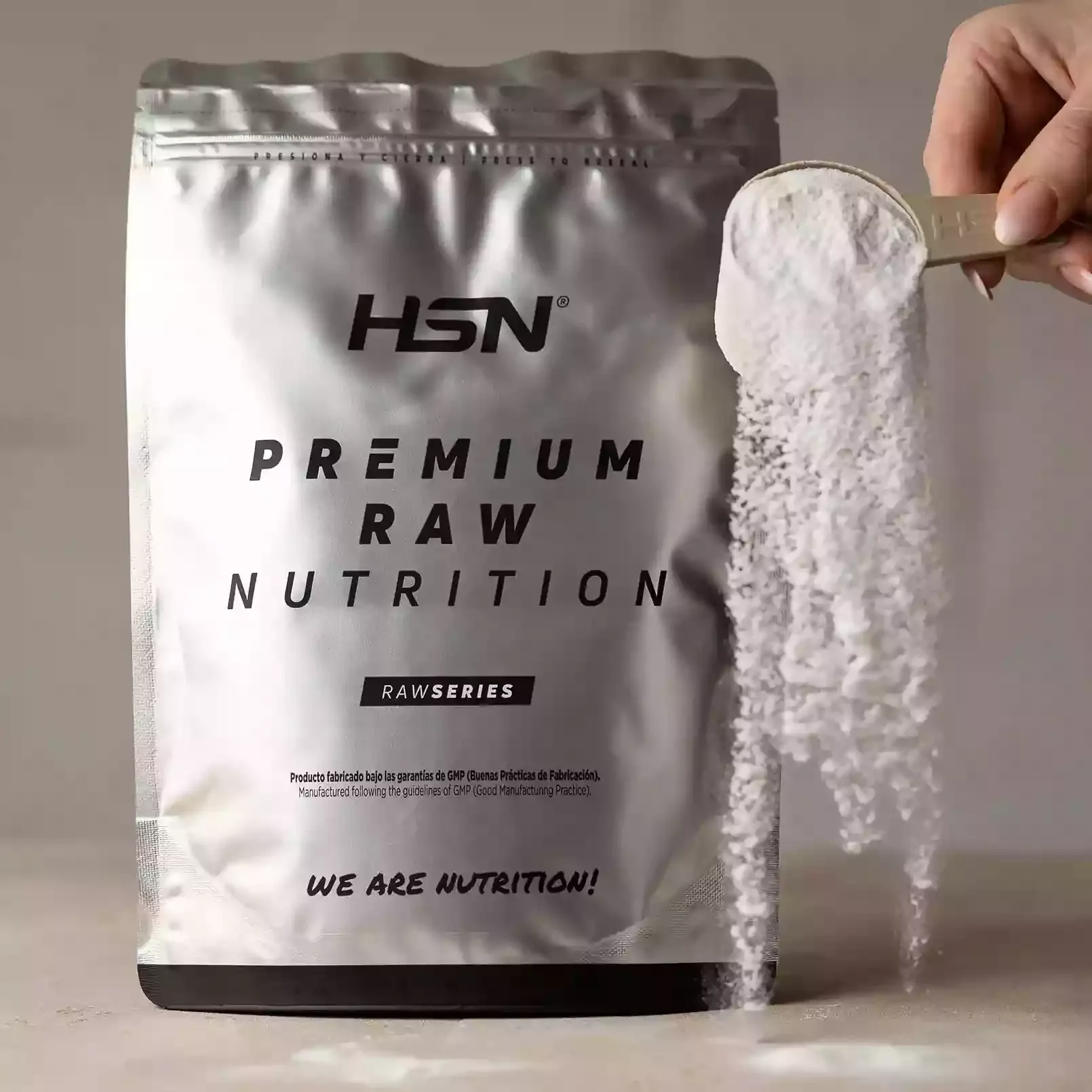 Saco prateado de suplemento em pó com escrita preta e mão a despejar pó branco.