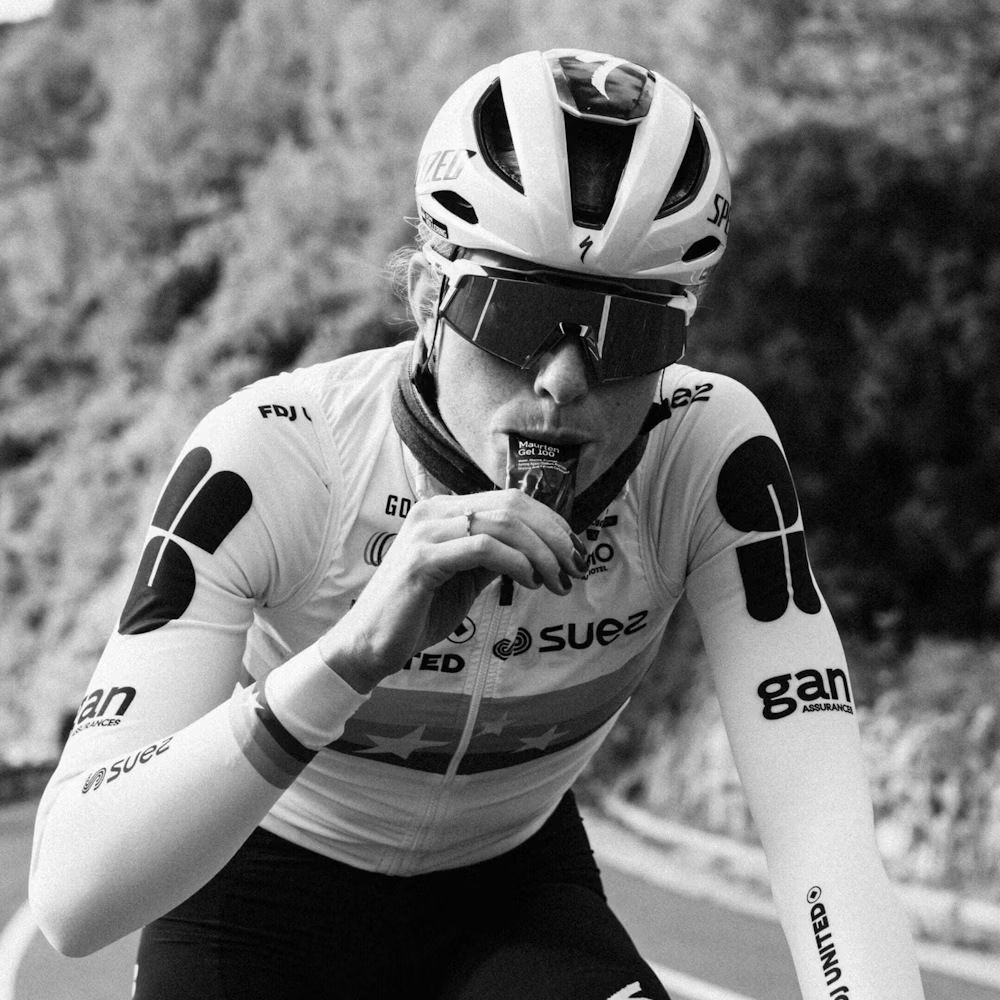Ciclista com capacete branco e óculos escuros a consumir gel energético durante pedalada na estrada
