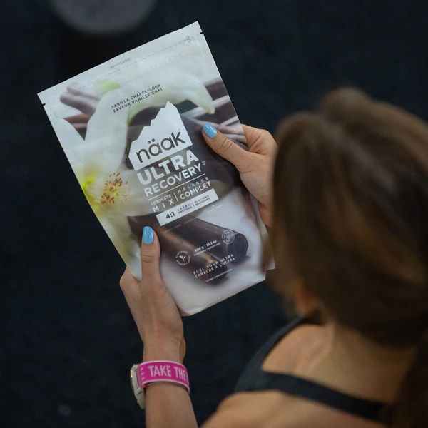 Embalagem de snack nääk Ultra Recovery com design branco e cinza, mãos femininas segurando o pacote.