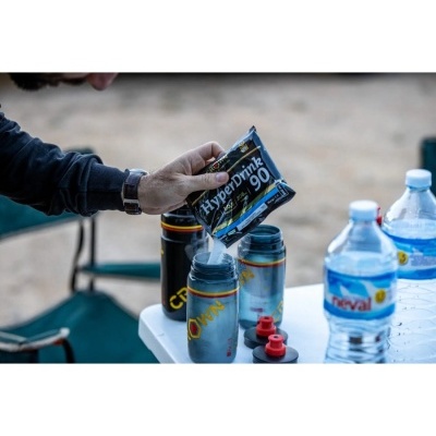 Pessoa a verter saqueta HyperDrink 90 em bidão prateado ao ar livre