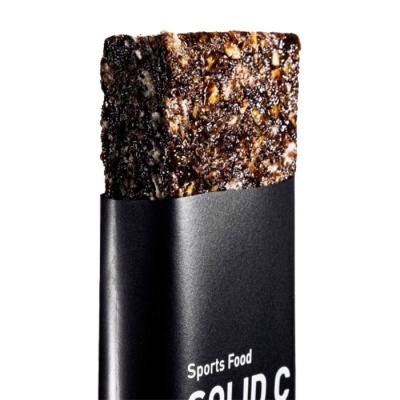 Barra energética castanha escura com sementes embalada em papel preto com texto branco