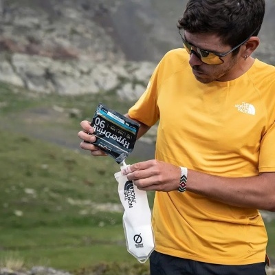 Homem a verter suplemento Hyporoman 90 para recipiente The North Face em montanha
