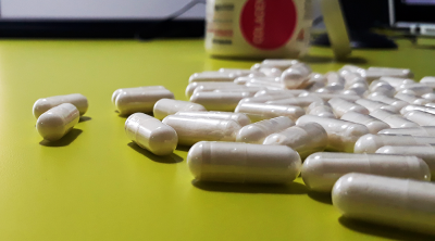 Frasco de suplementos e cápsulas brancas numa superfície amarela