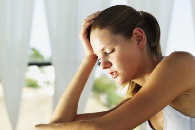 Mulher com camisola branca, mão na cabeça, interior iluminado pela luz do dia