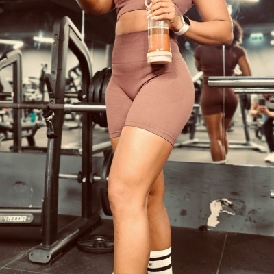 Mulher em roupa desportiva rosa clara segura suplemento e garrafa em ginásio com equipamentos e espelho