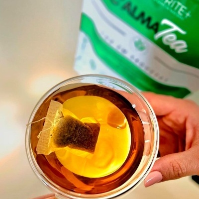 Chávena transparente com chá e saquinho de chá, mãos segurando, embalagem verde atrás