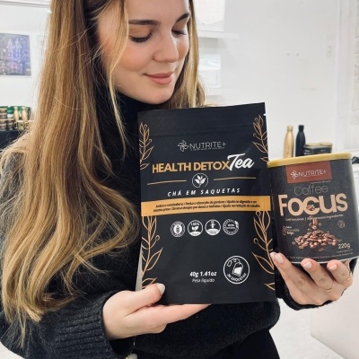 Mulher segurando chá Health Detox Tea e café Coffee Focus com embalagem preta e dourada