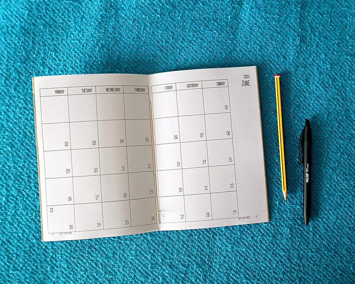 Agenda Mensal 2027 Calendário mensal aberto para junho em fundo azul com lápis e caneta ao lado