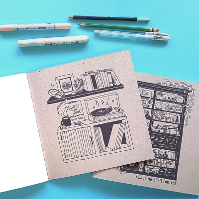 Dois cadernos com capas ilustradas, canetas e lápis sobre superfície azul