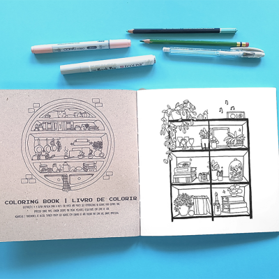 Livro de colorir aberto com desenhos de prateleiras ao lado de canetas e lápis sobre fundo azul